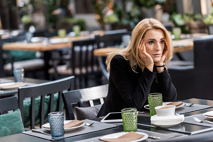 Woman sitting at a restaurant table, looking concerned.