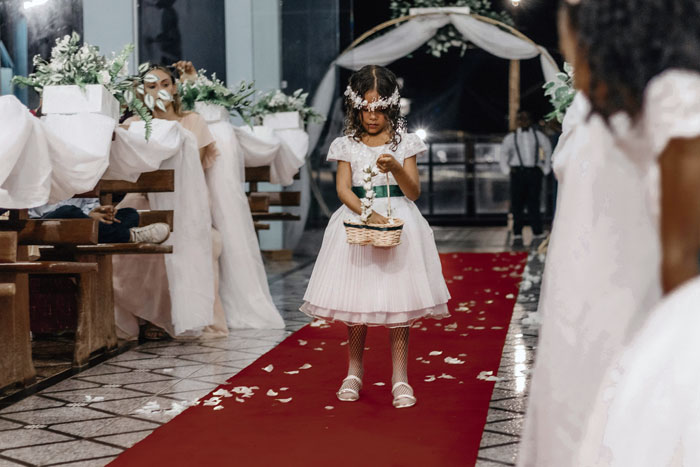 Young flower girl in white dress walking down wedding aisle, highlighting child-free wedding plans and travel costs.
