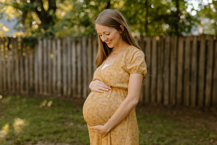 Pregnant woman in yellow dress smiling outdoors, representing heartless ex furious with pregnant wife situation.