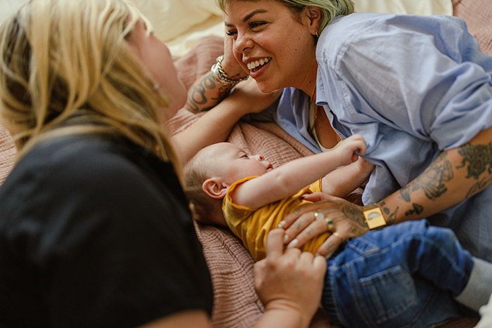 A couple lies on a bed smiling at their baby, highlighting IVF and family bonding moments.