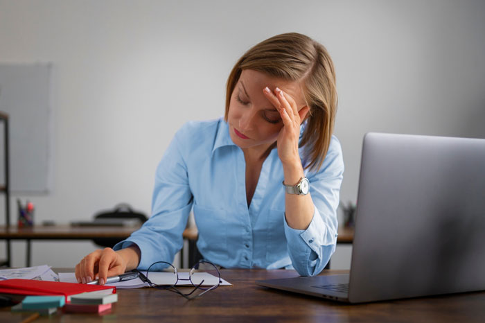 Woman sitting at desk looking stressed and frustrated after coworker takes credit for her work at office.
