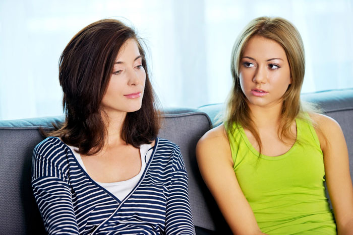 Two women sitting on a couch with tense expressions, illustrating sibling cut off and family pretending issues.