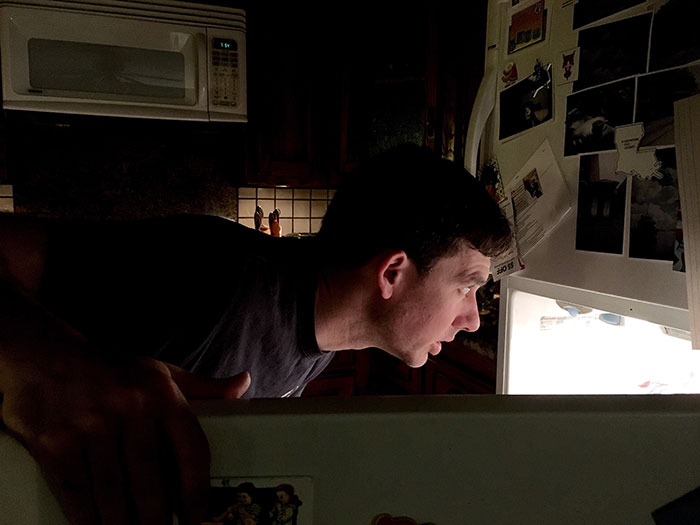 Man leaning over open refrigerator at night, reacting to the empty leftovers after his girlfriend ate them all.