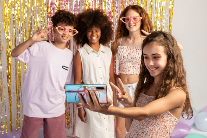 A 13-year-old girl taking a selfie with friends at a party, highlighting social drama and exclusion at school.