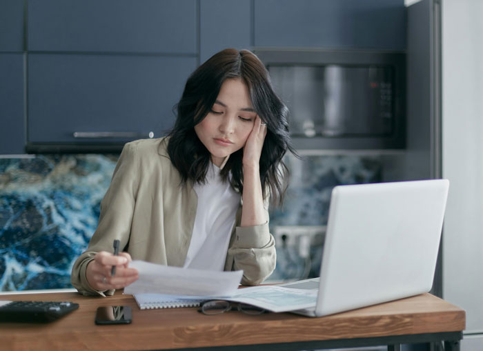 Young woman called poor by stepdad, looking thoughtful while reviewing documents and using a laptop at home.