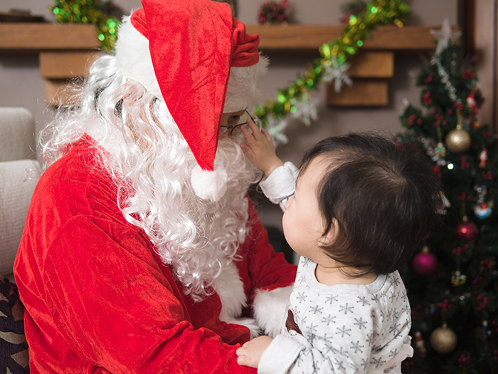 Baby reaching out to Santa Claus sitting by Christmas tree during festive holiday celebration indoors.