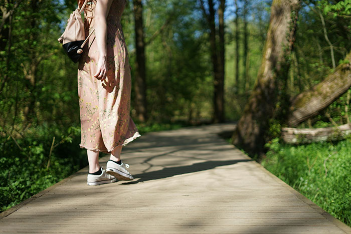 Woman walking on a wooden path in a forest wearing sneakers and a floral dress, illustrating avid walker doing 20K steps daily.